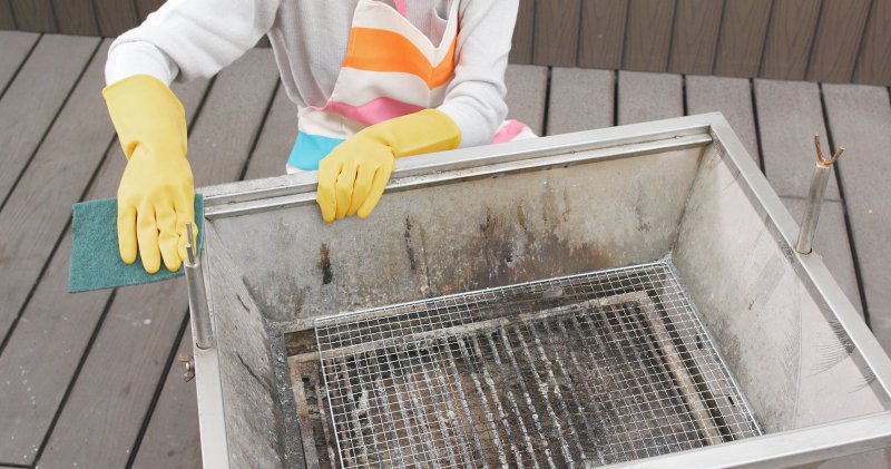 Frau putzt schmutzigen Grill mit Lappen und Handschuhen.