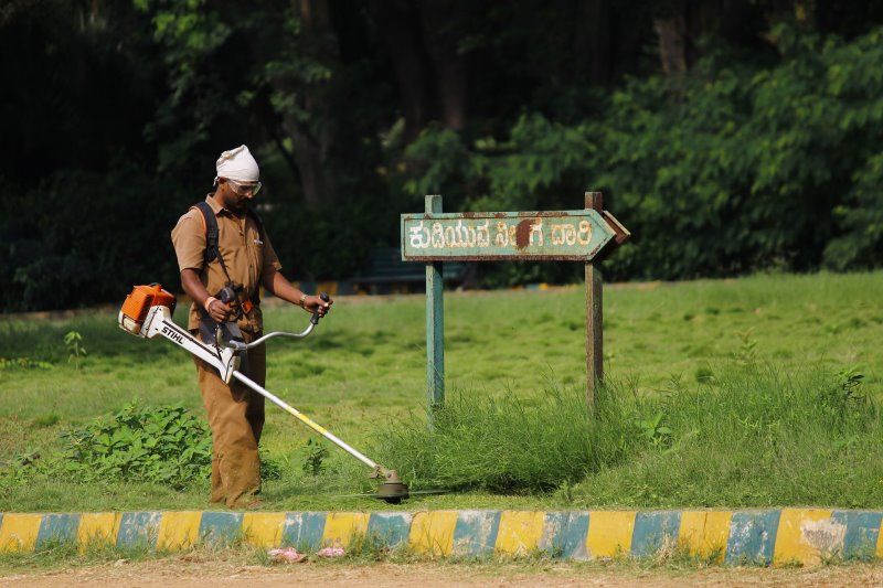 Rasentrimmer in Indien und Mann mit Schutzbrille Ein Mann trimmt den Rasen mit einer Motorsense in Indien